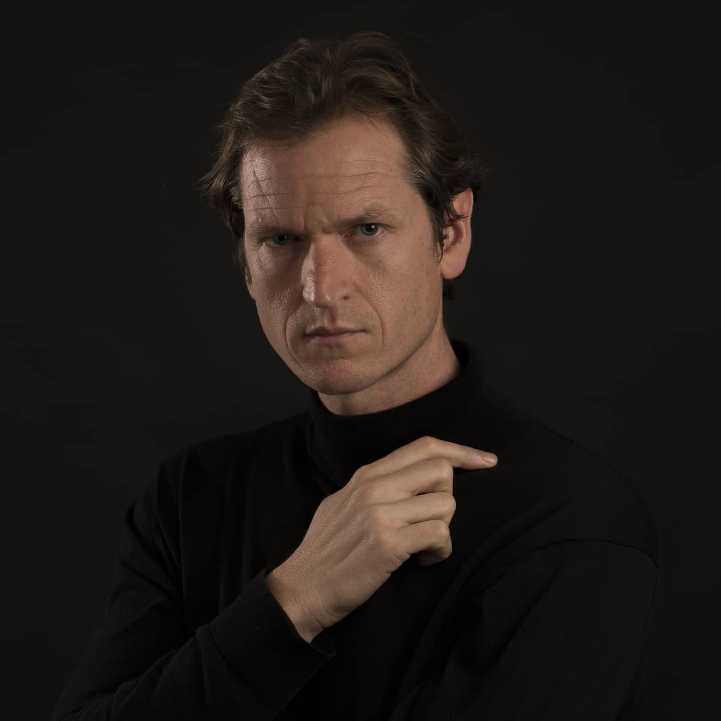 Retrato profesional de Timothy Cordukes con cuello alto negro sobre fondo oscuro